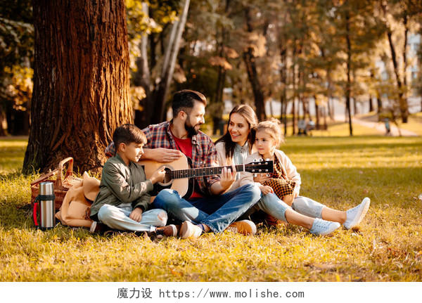年轻男子玩上一把吉他坐在一张野餐毯子幸福一家人幸福家庭幸福的人